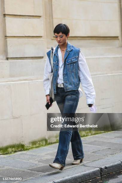 Model wears a gold pendant necklace, a white shirt, a blue denim sleeveless jacket, a black leather shoulder bag, a white shoulder bag, blue faded...