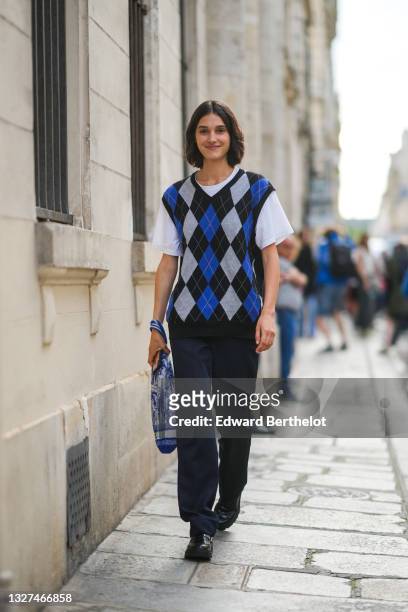 Model wears a white t-shirt, a black / blue and pale gray checkered jacquard print pattern sleeveless pullover, black pants, a blue and white print...