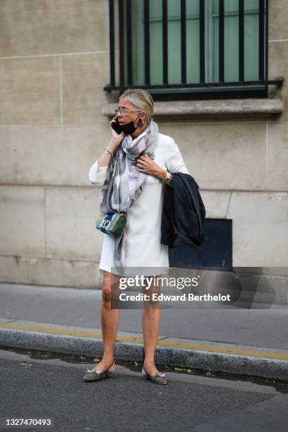 Guest wears glasses, a gray and white checkered pattern scarf from Christian Dior, silver bracelet, a white long sleeves short dress, a black blazer...