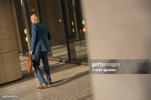 a young fit businessman in a classic blue suit with a leather laptop bag in his hand stopped between the columns of the business center - classic day 1 bildbanksfoton och bilder