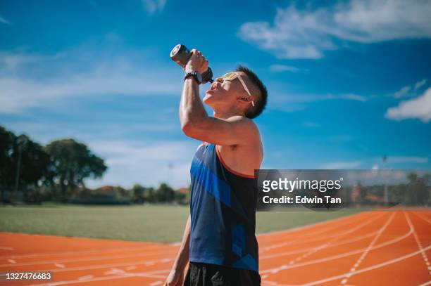 atleta deportivo masculino con gafas de sol bebiendo agua en el estadio de atletismo para todo tipo de clima por la mañana - all weather running track fotografías e imágenes de stock