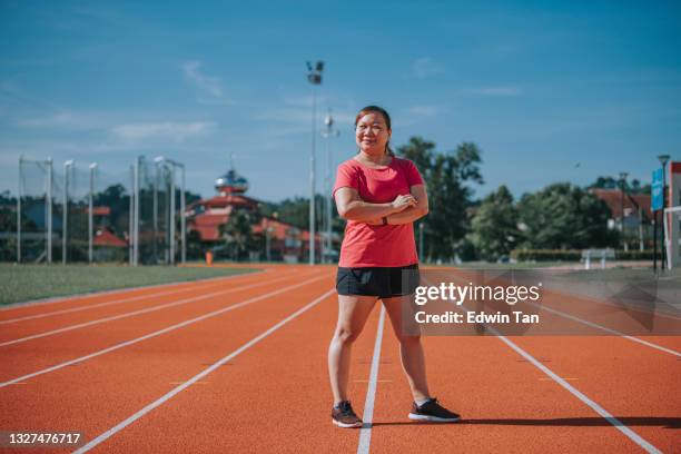 confianza satisfecha cuerpo positivo brazos de atleta femenina cruzada mirando a la cámara sonriendo de pie en todo el tiempo de atletismo y el estadio de campo en la mañana - all weather running track fotografías e imágenes de stock