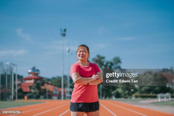 confidence satisfied body positive female athlete arms crossed looking at camera smiling standing on all-weather-track and field stadium in the morning - all weather running track stock pictures, royalty-free photos & images