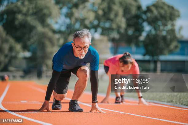 asian chinese senior couple getting ready to sprint at track and field stadium in the morning - forward athlete stock pictures, royalty-free photos & images