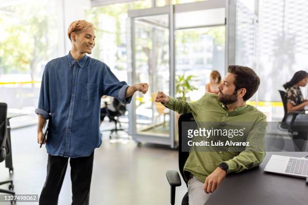 office colleagues greeting each other with fist bump - fist bump fotografías e imágenes de stock