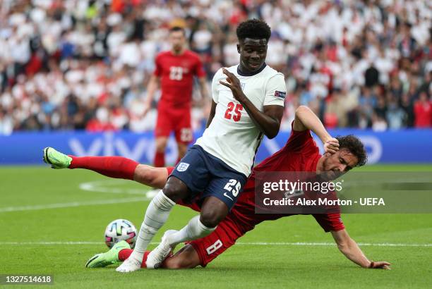 Bukayo Saka of England is challenged by Thomas Delaney of Denmark during the UEFA Euro 2020 Championship Semi-final match between England and Denmark...