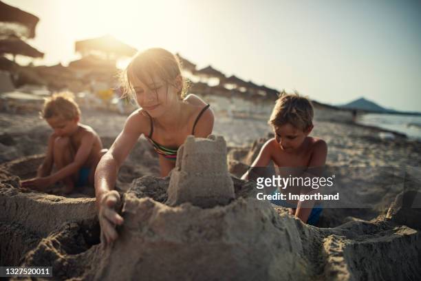 three kids enjoying building sandcastle on beach - sandcastle stock pictures, royalty-free photos & images