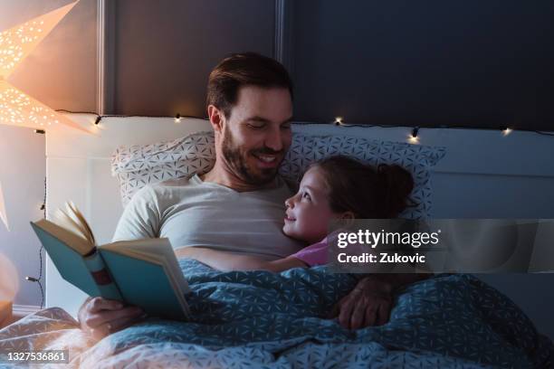 father reading a book for his daughter at night time - storytelling children stock pictures, royalty-free photos & images