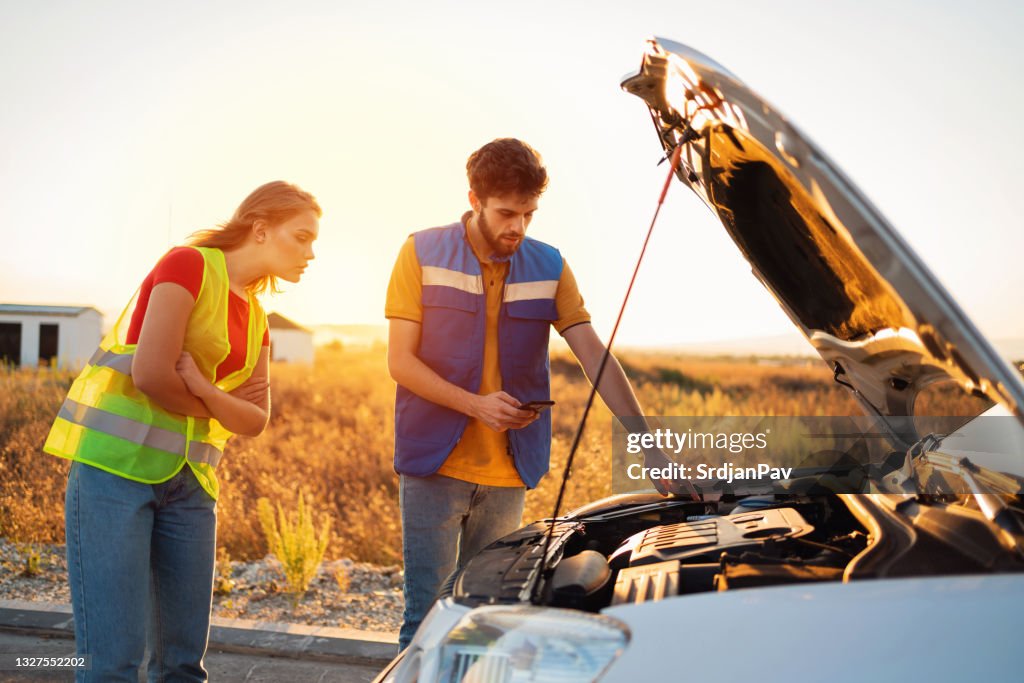 Service worker helping a young woman with a broken car on the road