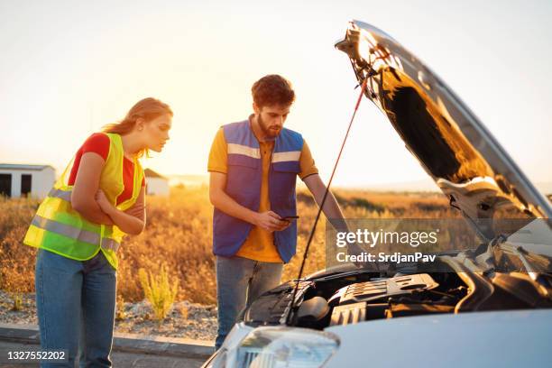 service worker helping a young woman with a broken car on the road - roadside assistance stock pictures, royalty-free photos & images