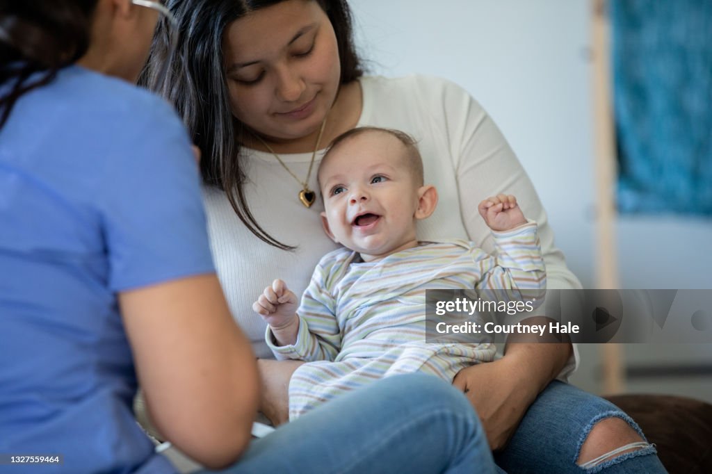 Baby lächelt, während es von einer Krankenschwester oder einem Arzt während einer Hausanruf-Ärztlichen Untersuchung untersucht wird