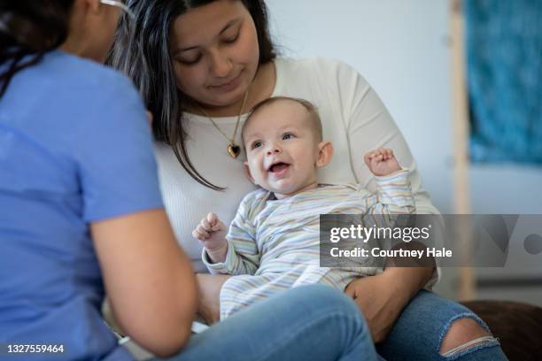 baby lächelt, während es von einer krankenschwester oder einem arzt während einer hausanruf-ärztlichen untersuchung untersucht wird - doctor and baby stock-fotos und bilder