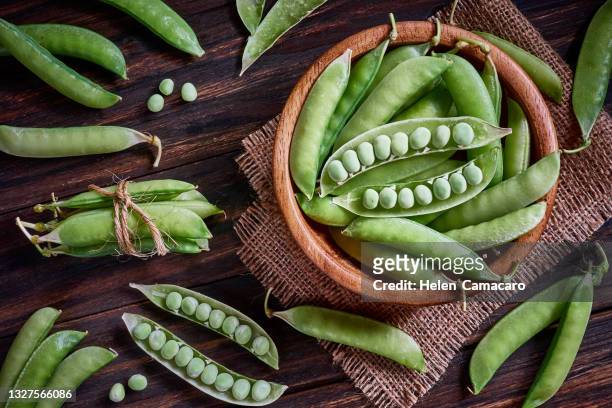 fresh green peas on rustic wooden table - bean stock-fotos und bilder