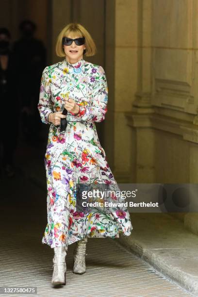 Anna Wintour wears black sunglasses, a white with multicolored flower print pattern long sleeves / turtleneck / long flowing dress from Balenciaga,...