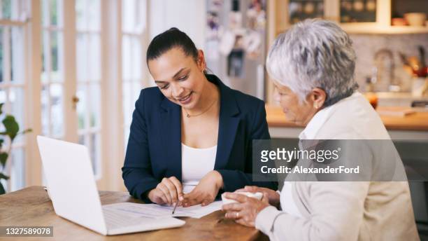 shot of a consultant going through paperwork during a meeting with a senior woman at home - insurance stock pictures, royalty-free photos & images