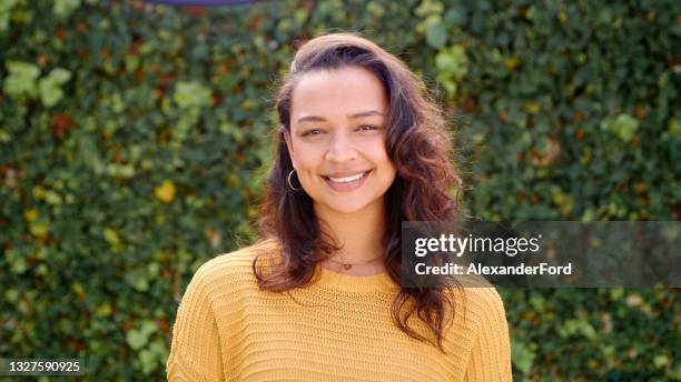 shot of an attractive young woman standing alone against a hedge in her garden during the day - portrait background stockfoto's en -beelden