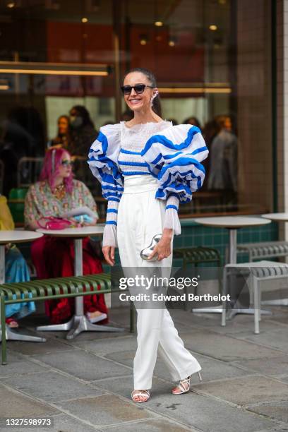 Guest wears a silver and crystals pendant large earring, black sunglasses, a white with blue striped ruffled large puffy long sleeves t-shirt, white...