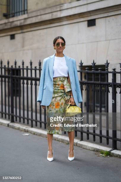 Guest wears black sunglasses, a white t-shirt, a pale blue checkered pattern long blazer jacket, gold necklaces, gold earrings, a silver bracelet, a...