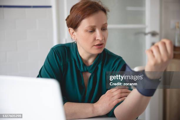 frau, die den blutdruck zu hause überprüft und mit vorfreude auf den monitor schaut - wrists stock-fotos und bilder