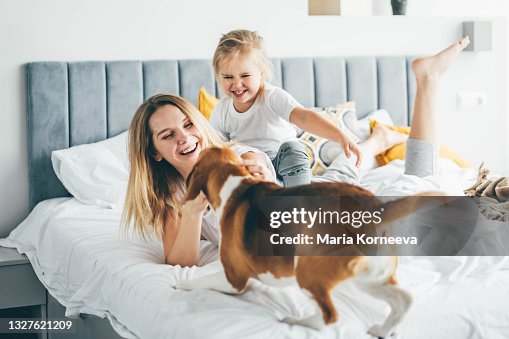 Happy mother and daughter with dog having fun and playing together on the bed at home. Happy mother and daughter with dog having fun and playing together on the bed at home.