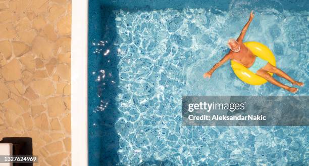 senior mann auf aufblasbarem ring im schwimmbad - schwimmring stock-fotos und bilder