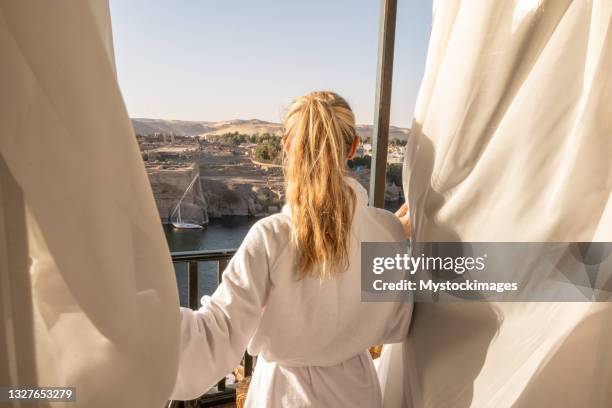 woman opening curtains in hotel room at sunrise, nile river - green curtain stock pictures, royalty-free photos & images