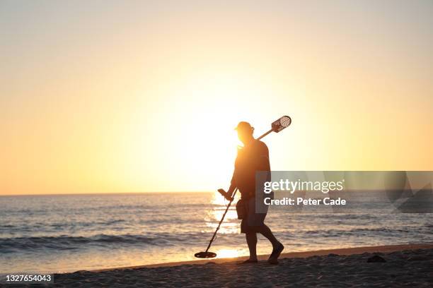 man on beach with metal detector at sunset - schatzoeken stockfoto's en -beelden