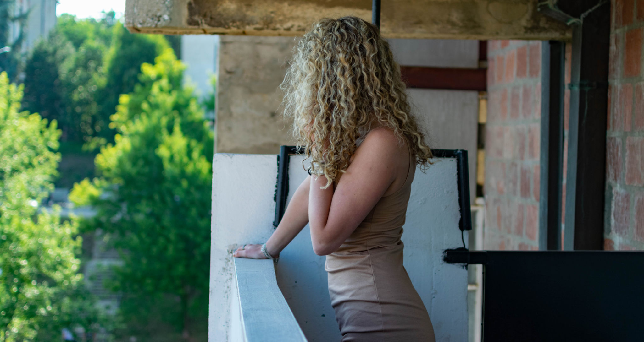 Beautiful young woman with curly hair, siting at her home, at her balcony, lying down and using her smartphone to connect with her friends, smiling and enjoing her free time, relaxing with coffee and cookies. Beautiful young woman with curly hair, siting at her home, at her balcony, lying down and using her smartphone to connect with her friends, smiling and enjoing her free time, relaxing with coffee and cookies.