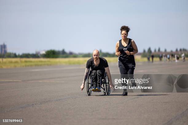 man in wheelchair exercising with female on an airstrip - tempelhof airport stock pictures, royalty-free photos & images