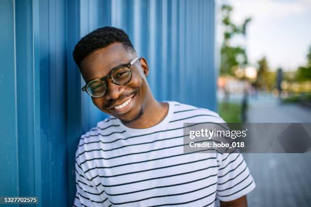 young, cheerful black man on blue door background - striped shirt stock pictures, royalty-free photos & images
