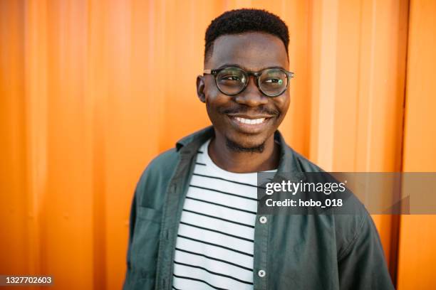 young, cheerful black man leaning on orange door background - portrait orange background stock pictures, royalty-free photos & images
