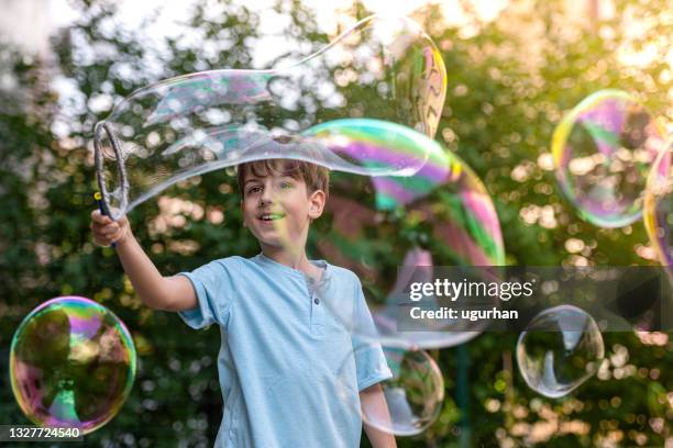 un petit garçon joue dans le jardin arrière avec une baguette à bulles géante. - bain moussant photos et images de collection