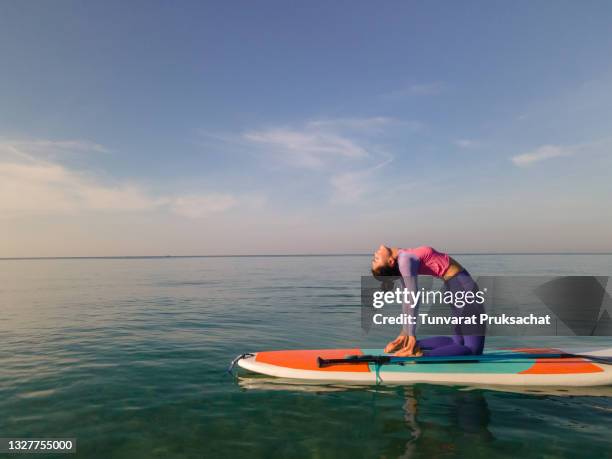 young woman practicing yoga on a paddleboard . - yoga retreat stock pictures, royalty-free photos & images