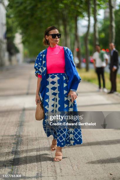 Guest wears black sunglasses, gold pendant earrings, a fuchsia pink ribbed turtleneck long sleeves t-shirt, a blue with white print pattern oversized...