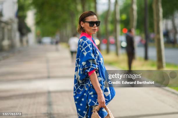 Guest wears black sunglasses, gold pendant earrings, a fuchsia pink ribbed turtleneck long sleeves t-shirt, a blue with white print pattern oversized...
