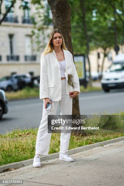 Guest wears earrings, a gold chain necklace, a white blazer jacket, white matching pants, a white crop-top, a beige and brown Dior vintage crossbody...