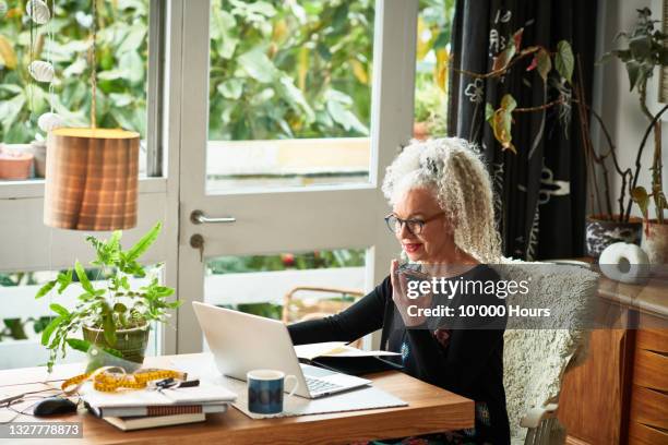 cheerful senior businesswoman speaking on smart phone in front of laptop - disrupt aging stock pictures, royalty-free photos & images