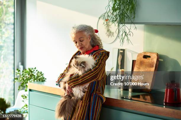 senior woman cuddling pet cat in kitchen - hairy woman stockfoto's en -beelden