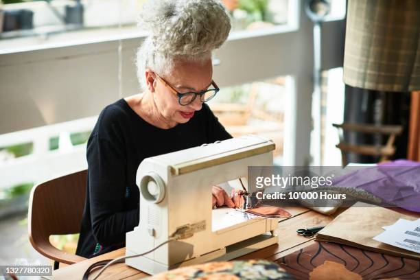 mature woman stitching material on electric sewing machine - frau nähen stock-fotos und bilder