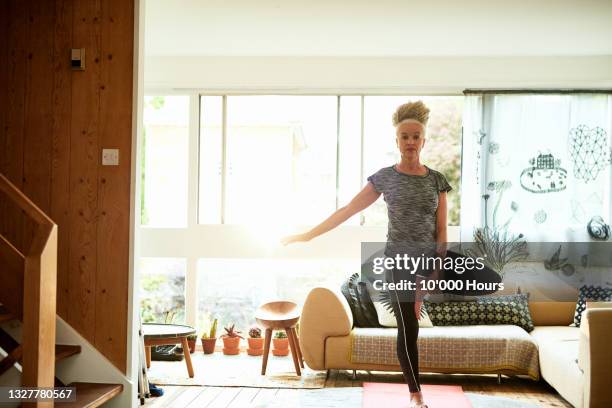 senior woman standing on one leg in living room - tree position stock pictures, royalty-free photos & images