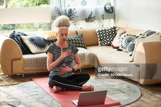 grey haired woman concentrating on breathing exercises at home - breathing exercise stockfoto's en -beelden