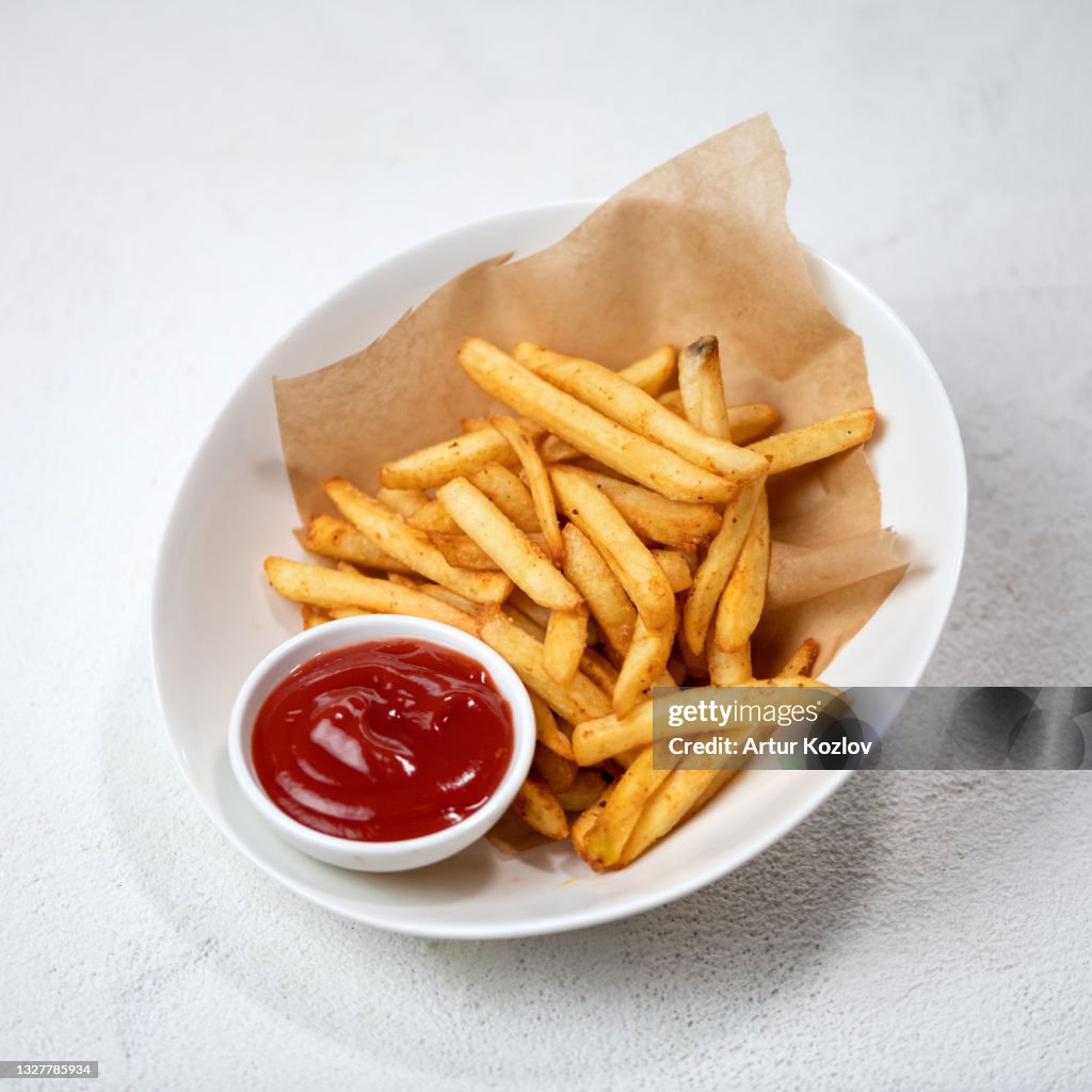 Fried potatoes with tomato sauce, fries with ketchup. Food plate isolated on white background