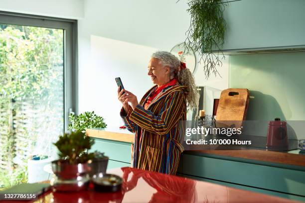 smiling grey haired woman speaking on video call - smartphone zuhause stock-fotos und bilder