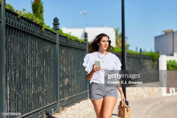 woman walking on the street with smartphone in hand - shorts stock pictures, royalty-free photos & images