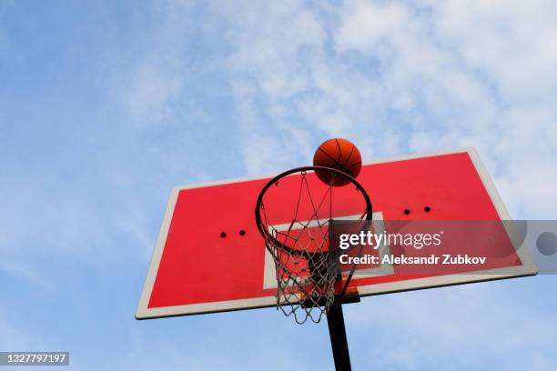 a basketball flies into the basket, against the blue sky, in an open area. theme of sports, achievement of goals. - patio de edificio fotografías e imágenes de stock