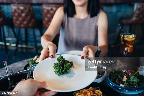 young asian couple enjoying dinner date in a restaurant. sharing fresh green salad across the table during meal. eating out lifestyle - passa foto e immagini stock