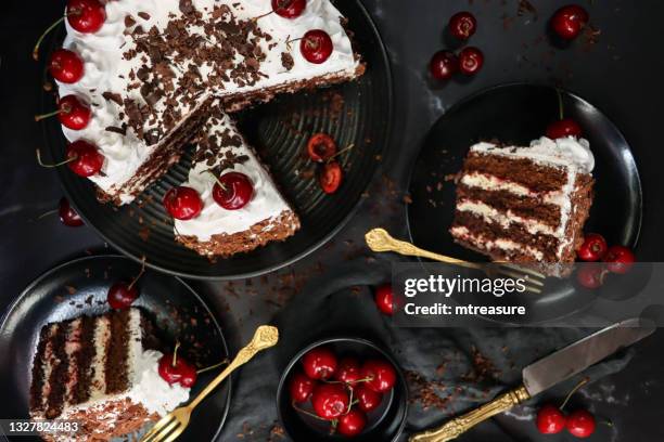 image of sliced black forest gateau with piped whipped cream rosettes with morello cherries, luxury chocolate cake frosted with whipped cream and covered with chocolate shavings, black plate, black background, elevated view - gateaux bildbanksfoton och bilder