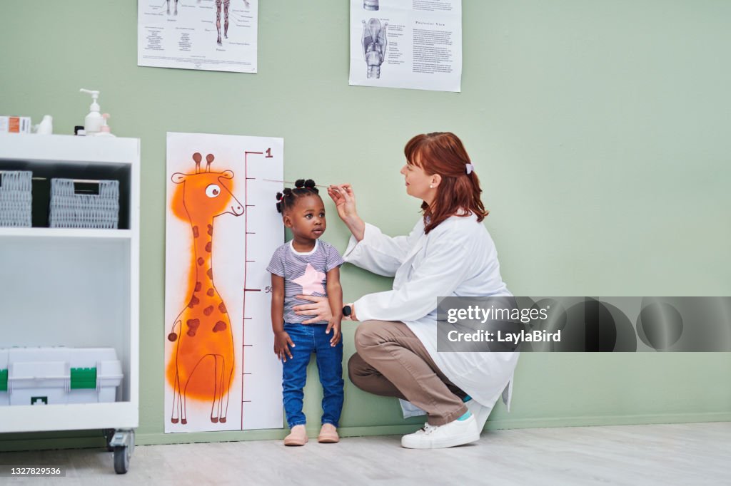 Shot of a doctor measuring an adorable little girl’s height during a consultation