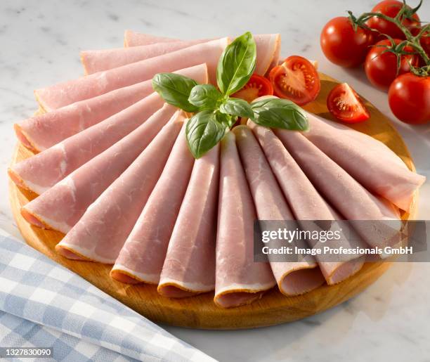 slices of honey roasted ham on a circular wooden cutting board with garnish of basil and tomatoes - honey ham stock pictures, royalty-free photos & images