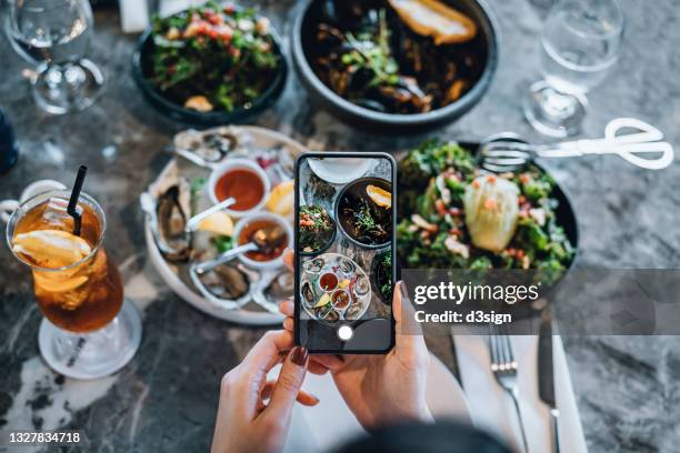 overhead view of young woman taking photos of scrumptious and delicious meal on dining table with smartphone before eating it in restaurant. eating out lifestyle. camera eats first culture - trends asian stock-fotos und bilder